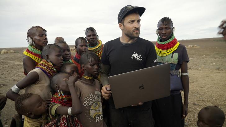 Saype, un ordinateur portable à la main, entouré de Kenyans, regarde au loin